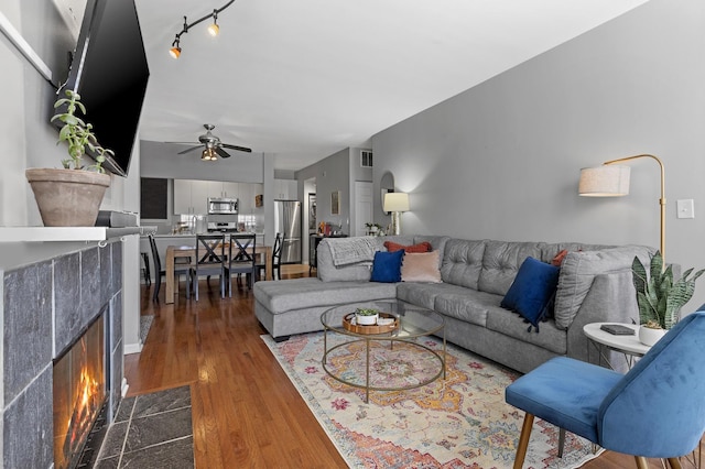 living area featuring a tile fireplace, visible vents, dark wood finished floors, and ceiling fan