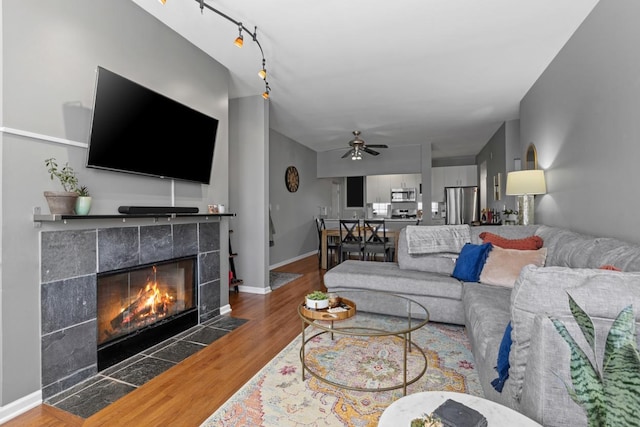 living area with baseboards, a tiled fireplace, a ceiling fan, and wood finished floors