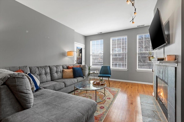 living room with light wood finished floors, visible vents, baseboards, a tiled fireplace, and rail lighting