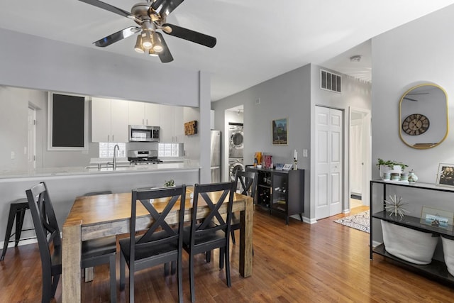 dining area with ceiling fan, visible vents, stacked washer / dryer, and wood finished floors