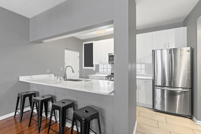 kitchen featuring stainless steel appliances, a breakfast bar, a peninsula, a sink, and white cabinetry