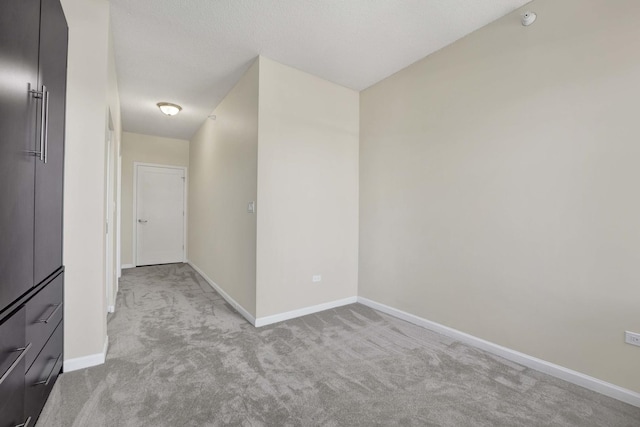 spare room featuring baseboards, a textured ceiling, and light colored carpet