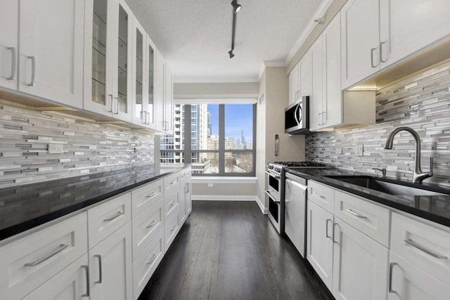 kitchen featuring a sink, white cabinetry, appliances with stainless steel finishes, glass insert cabinets, and crown molding