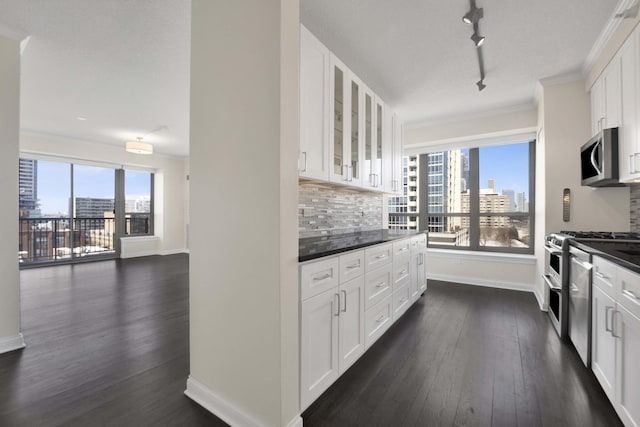 kitchen featuring appliances with stainless steel finishes, dark countertops, glass insert cabinets, and tasteful backsplash