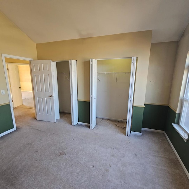 unfurnished bedroom with lofted ceiling, light carpet, baseboards, and two closets