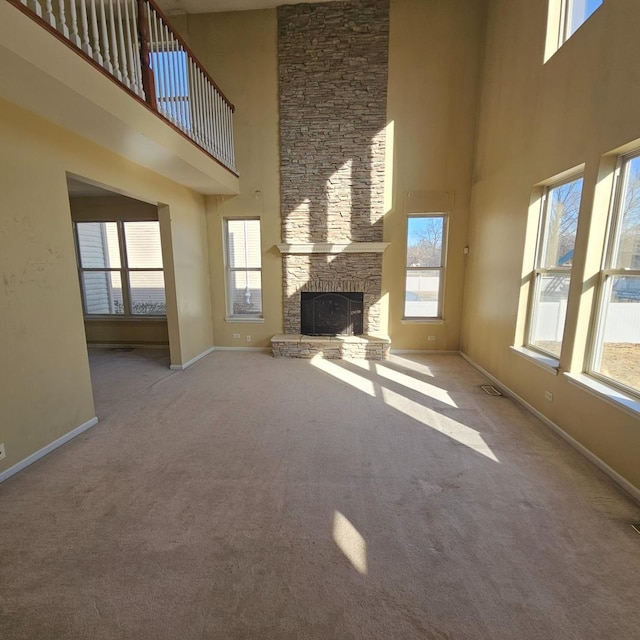 unfurnished living room with light carpet, a fireplace, a towering ceiling, and baseboards