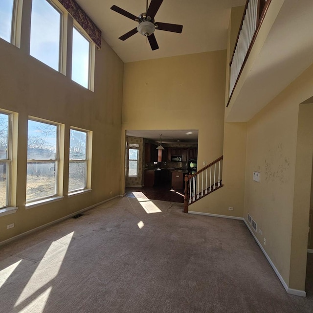 unfurnished living room featuring stairs, carpet floors, plenty of natural light, and baseboards