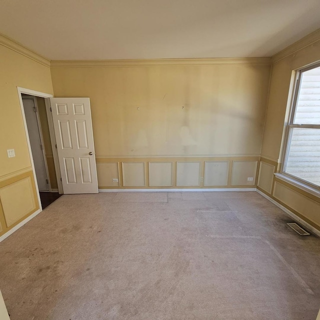 carpeted empty room featuring visible vents, crown molding, and a decorative wall