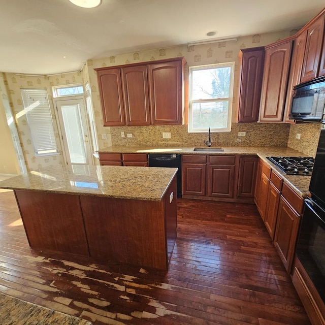 kitchen featuring tasteful backsplash, dark wood finished floors, light stone countertops, black appliances, and a sink