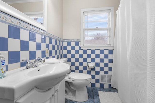 bathroom with tile walls, toilet, wainscoting, a sink, and tile patterned flooring