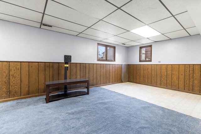 basement with wainscoting, wood walls, and a drop ceiling