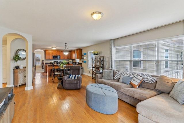 living room featuring light wood-style flooring, baseboards, and arched walkways