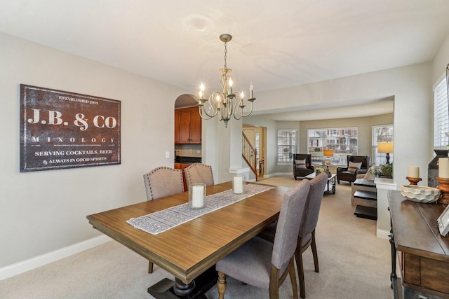 dining area with light carpet, baseboards, arched walkways, stairway, and an inviting chandelier