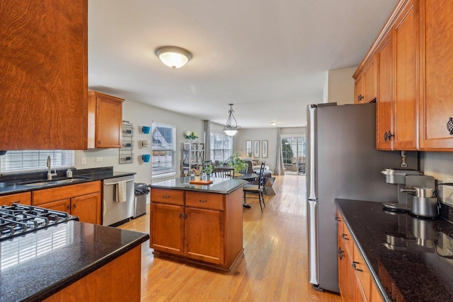 kitchen with brown cabinetry, appliances with stainless steel finishes, light wood-style floors, pendant lighting, and a sink