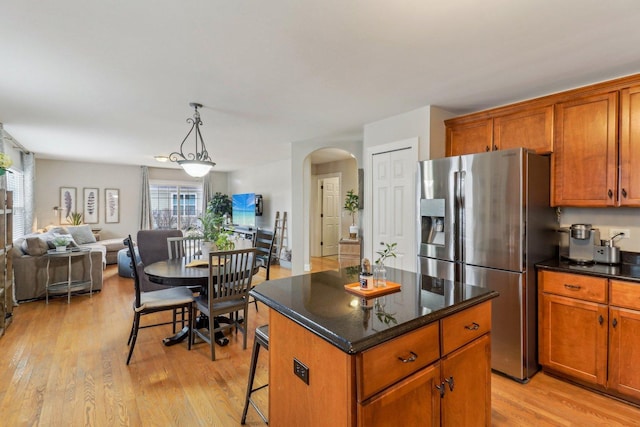 kitchen with arched walkways, stainless steel fridge with ice dispenser, open floor plan, a center island, and hanging light fixtures