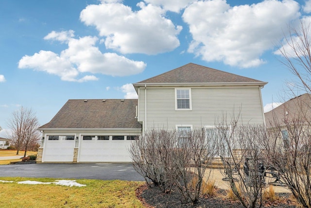 view of side of property with a garage, a shingled roof, and aphalt driveway