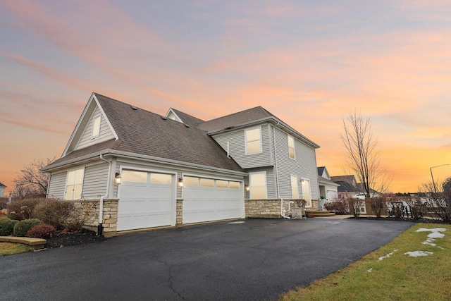 view of front of home with driveway, stone siding, an attached garage, and a shingled roof