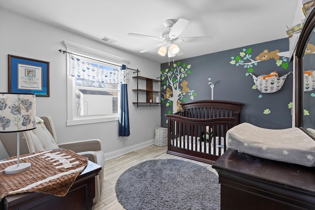 bedroom featuring light wood-style flooring, a ceiling fan, visible vents, baseboards, and a nursery area