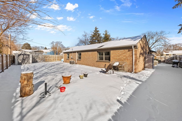 snow covered property featuring a fenced backyard and brick siding