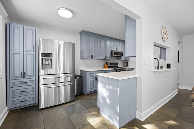 kitchen with gray cabinets, light countertops, decorative backsplash, appliances with stainless steel finishes, and baseboards