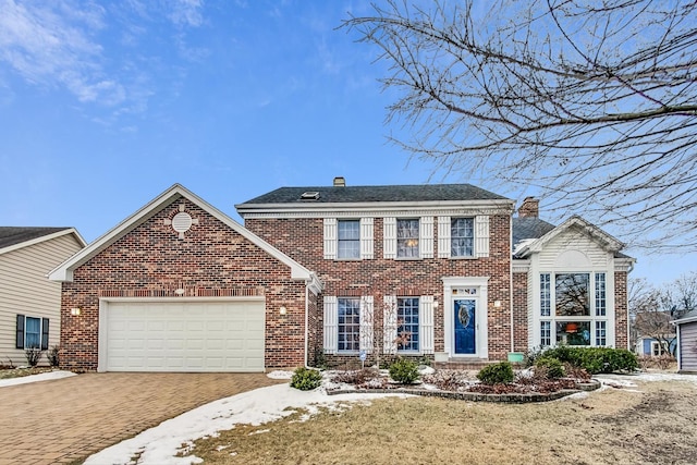 colonial inspired home featuring a garage, decorative driveway, and brick siding