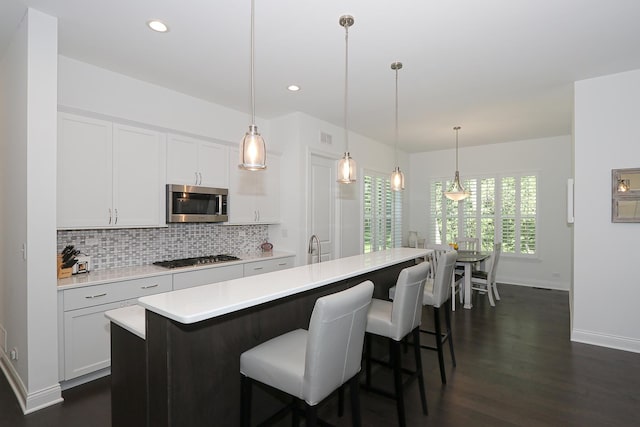 kitchen featuring pendant lighting, light countertops, appliances with stainless steel finishes, a kitchen island with sink, and white cabinets