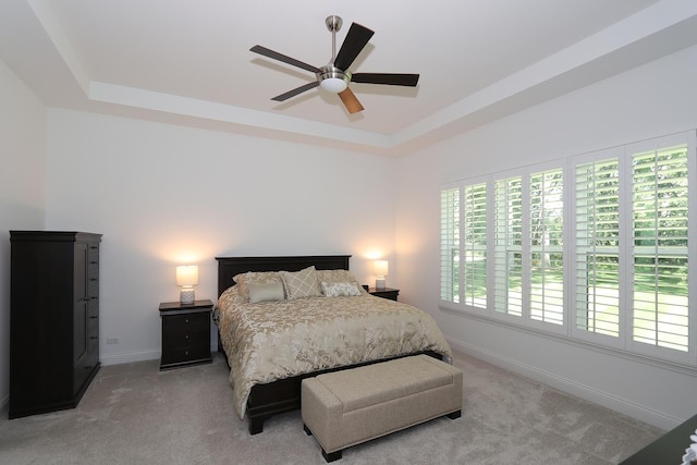 bedroom with a ceiling fan, a raised ceiling, light colored carpet, and baseboards