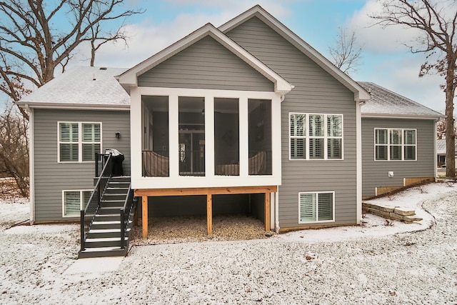 snow covered back of property with stairs and a sunroom