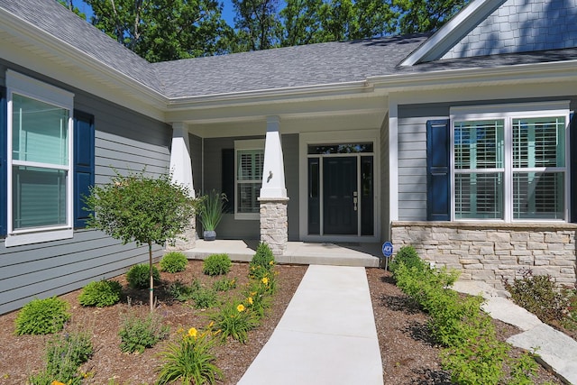 entrance to property with stone siding, covered porch, and roof with shingles