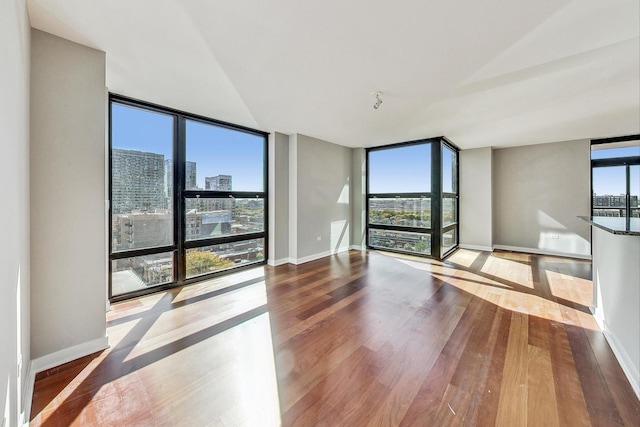 empty room with baseboards, a wall of windows, a city view, and wood finished floors