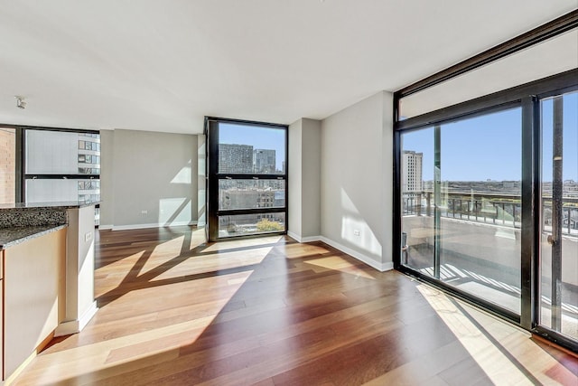 doorway with a view of city, a wall of windows, light wood-style flooring, and baseboards