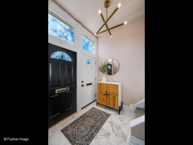 foyer with marble finish floor, baseboards, and an inviting chandelier