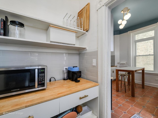 kitchen with dark tile patterned flooring, butcher block counters, baseboards, tasteful backsplash, and stainless steel microwave