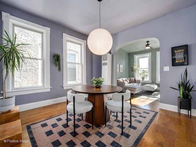 dining room with dark wood-type flooring, arched walkways, and baseboards