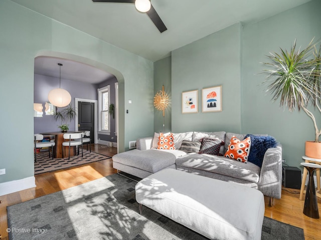 living area featuring a ceiling fan, baseboards, arched walkways, and wood finished floors