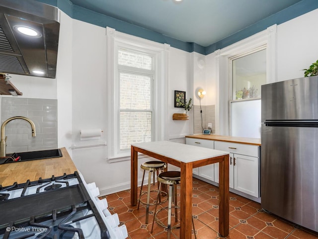 kitchen featuring white cabinets, wood counters, freestanding refrigerator, ventilation hood, and a sink