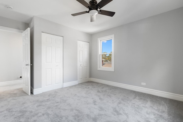 unfurnished bedroom with carpet flooring, baseboards, two closets, and ceiling fan