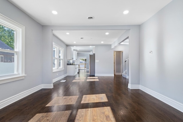 unfurnished living room featuring dark wood-type flooring, stairway, baseboards, and visible vents