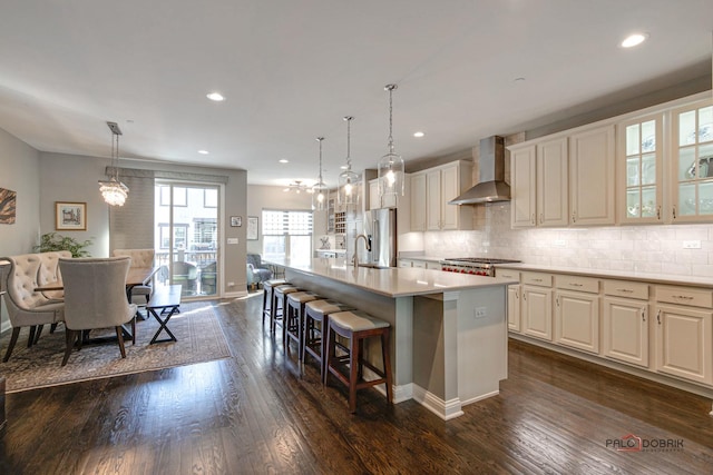 kitchen featuring a center island with sink, dark wood-style flooring, stainless steel appliances, wall chimney range hood, and backsplash