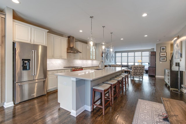 kitchen featuring a kitchen bar, high end fridge, fridge, wall chimney exhaust hood, and decorative backsplash