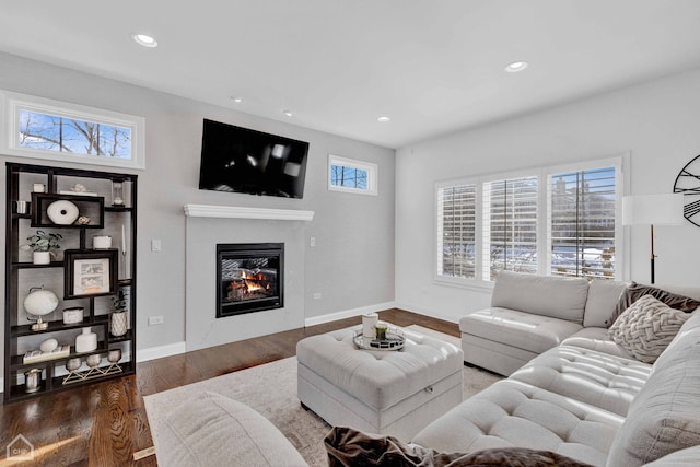 living area featuring a glass covered fireplace, baseboards, recessed lighting, and wood finished floors