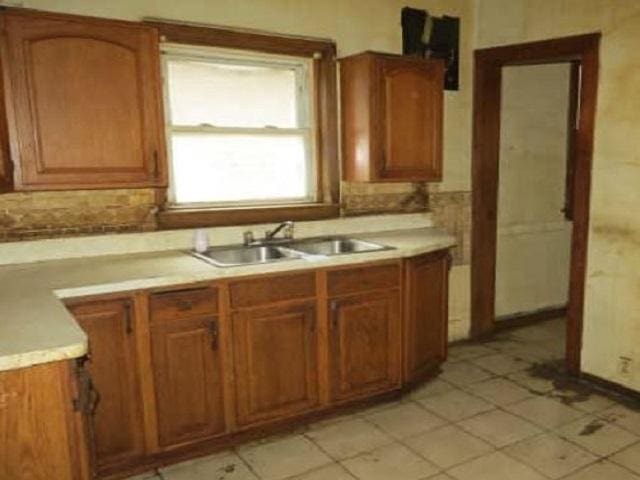 kitchen with brown cabinets, light countertops, a sink, and backsplash