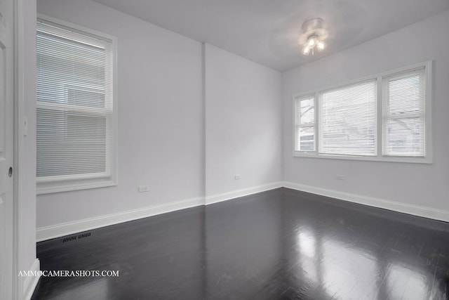 unfurnished room with dark wood-style flooring, visible vents, and baseboards