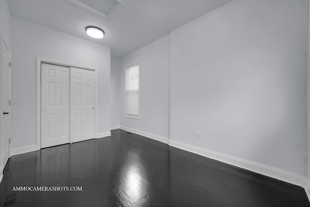 unfurnished bedroom with a closet, dark wood finished floors, attic access, and baseboards