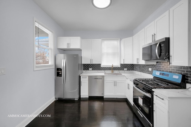 kitchen featuring baseboards, decorative backsplash, appliances with stainless steel finishes, white cabinetry, and a sink