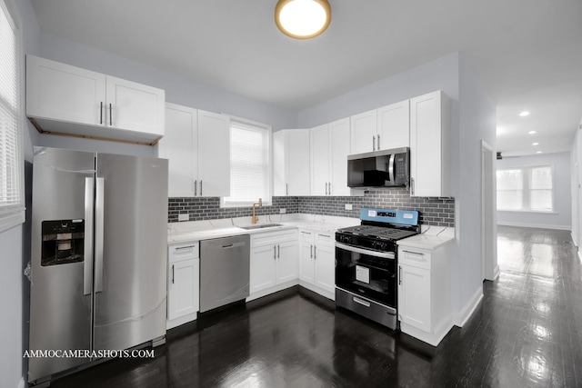 kitchen featuring tasteful backsplash, appliances with stainless steel finishes, dark wood-type flooring, white cabinets, and a sink