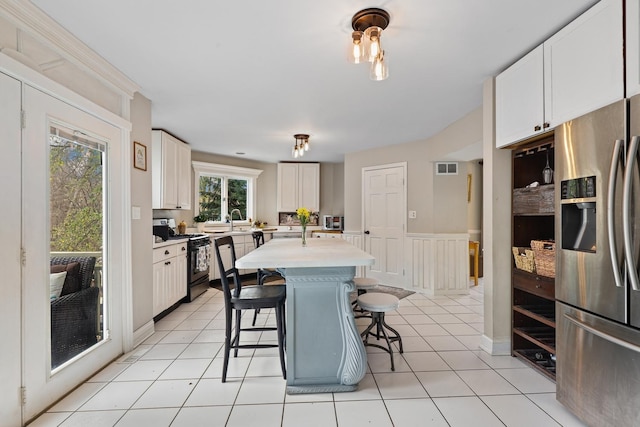 kitchen featuring a breakfast bar, white cabinetry, light countertops, stainless steel fridge, and gas range