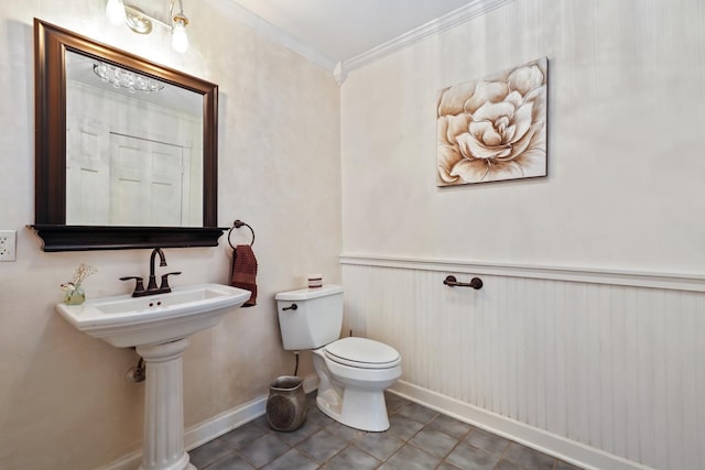 half bathroom featuring tile patterned flooring, toilet, a wainscoted wall, baseboards, and ornamental molding