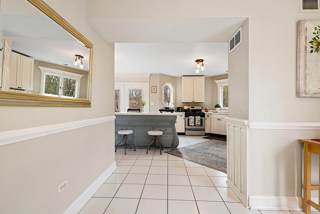 interior space featuring light tile patterned floors, stainless steel gas range oven, visible vents, baseboards, and light countertops