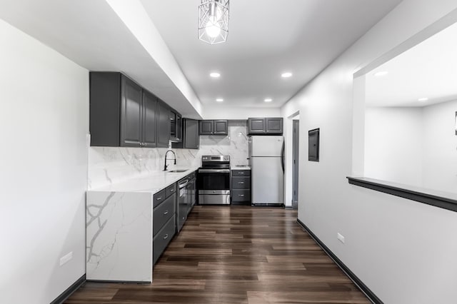 kitchen with appliances with stainless steel finishes, dark wood-style flooring, a sink, gray cabinets, and backsplash